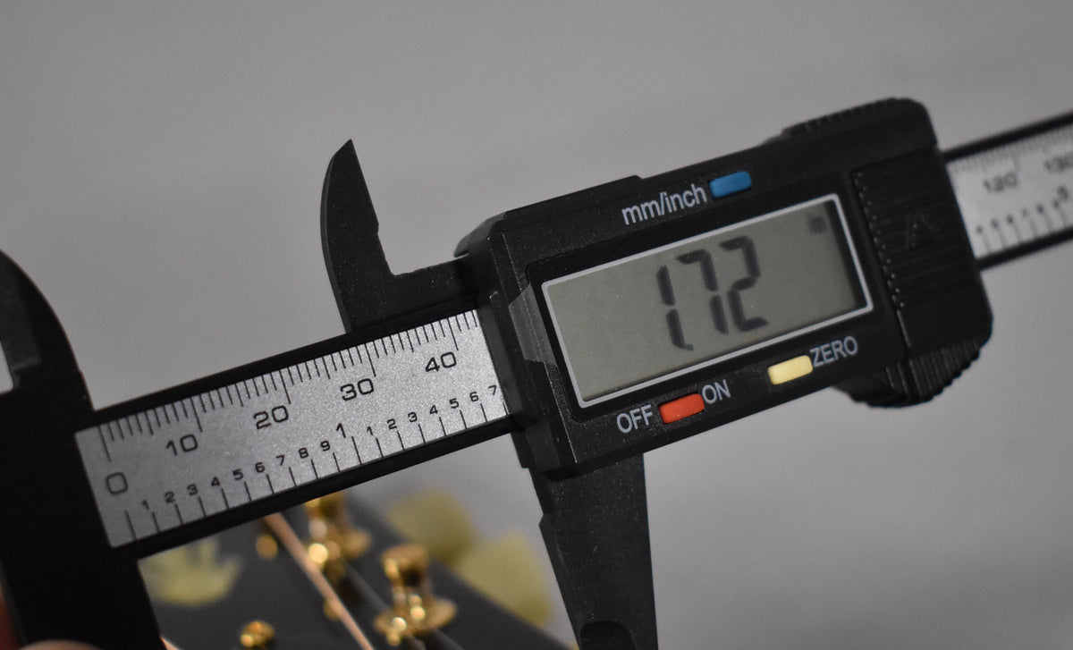 A digital caliper measures 17.2mm across the guitar's nut, with gold tuning pegs visible below.