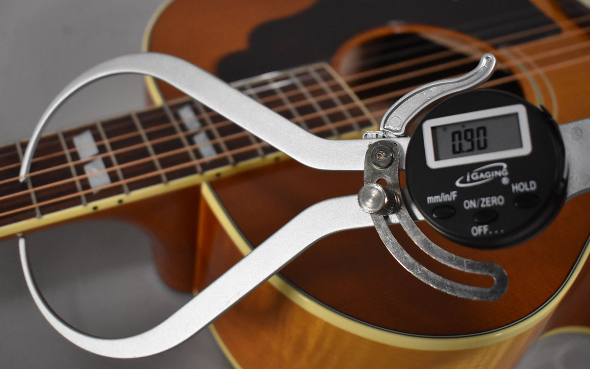 A digital caliper measures the guitar's body depth at 0.90, with the sunburst finish and fretboard visible.