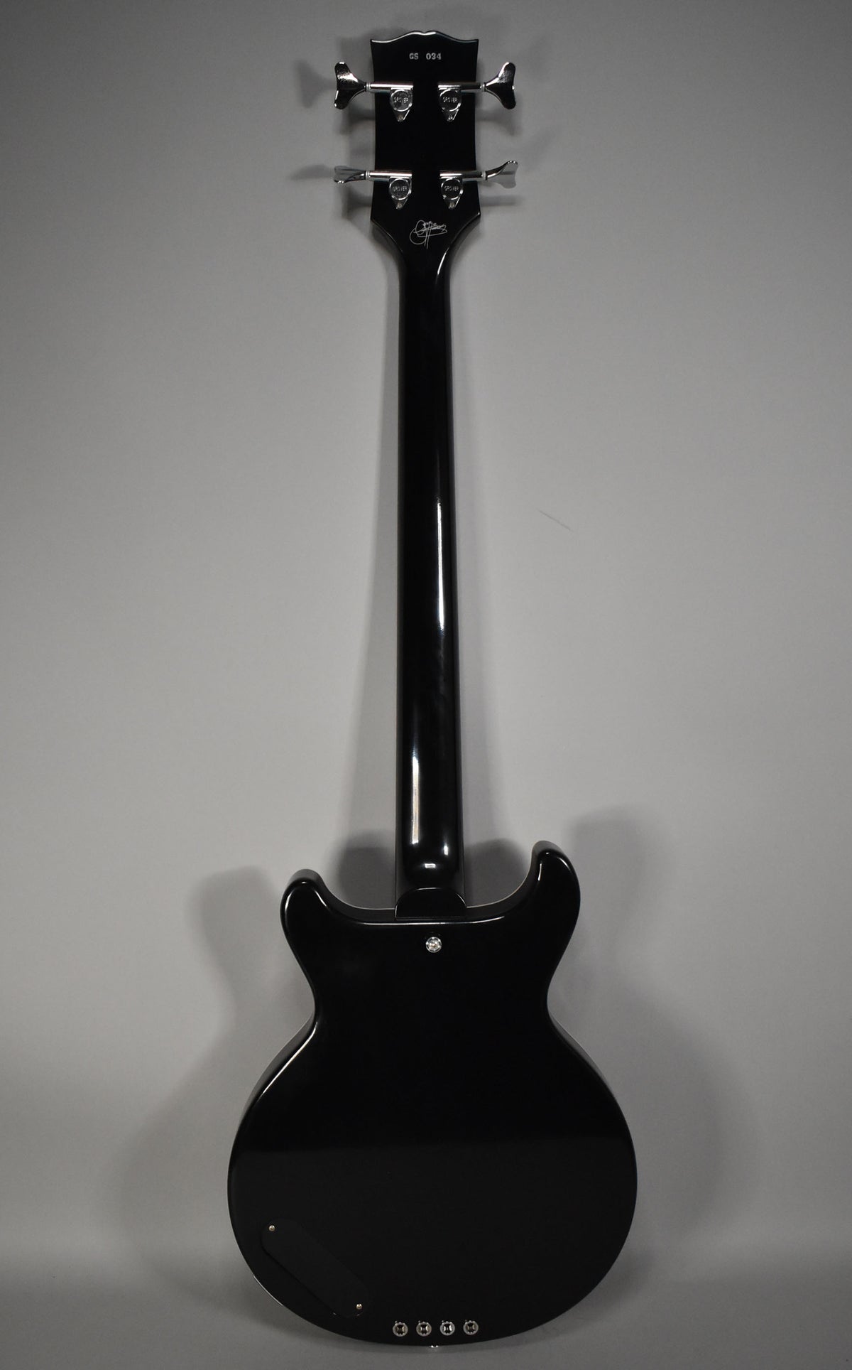 The full rear view of a glossy black bass, showing the headstock with four chrome tuners, neck, and body with a control plate.