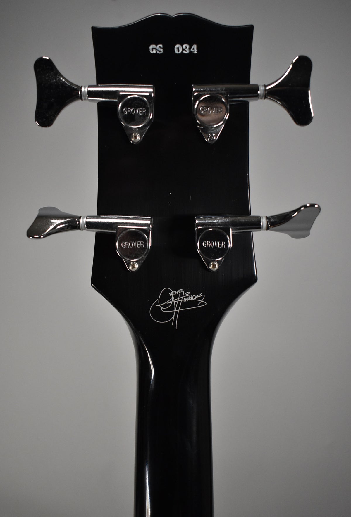 The back of the glossy black headstock and upper neck, showing four chrome tuners and a white Gene Simmons signature.