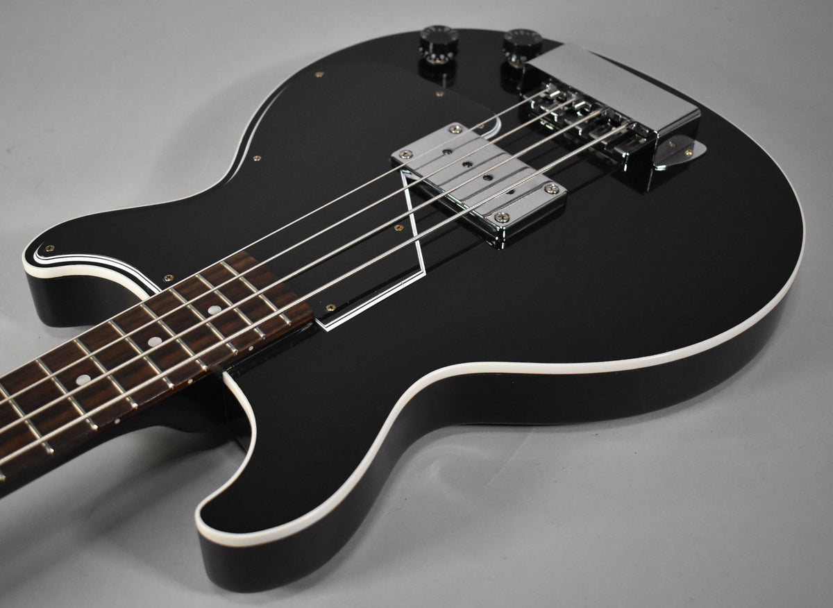 The glossy black bass is angled from the lower bout, showing the chrome bridge cover, pickup, and two black control knobs.