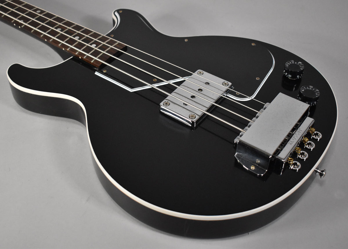 Close-up of the glossy black bass body, showing the chrome bridge cover, pickup, and two black control knobs.