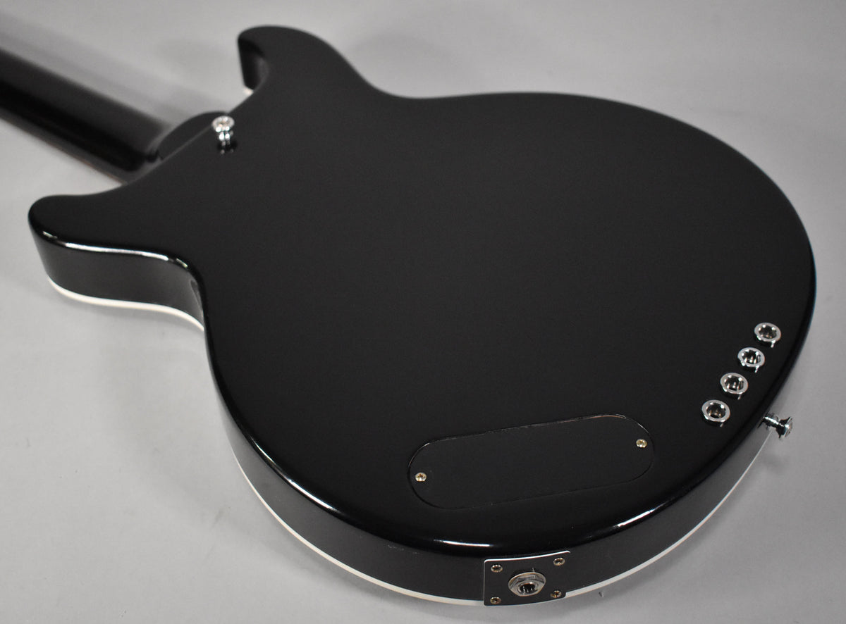 The back of the glossy black bass body, with white binding, shows a control cavity cover, output jack, and four string ferrules.
