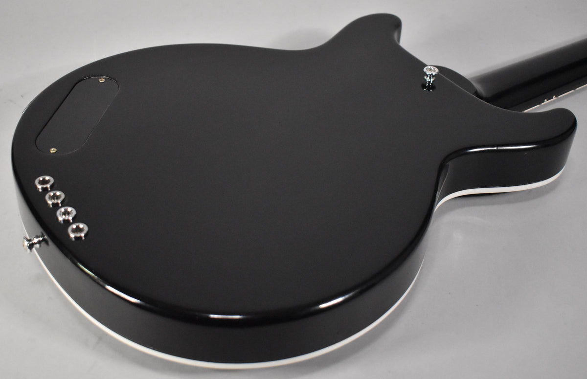 The back of a black bass guitar with white binding, showing the control cavity cover, strap button, and string ferrules.
