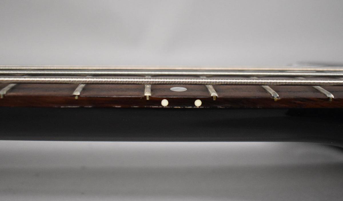 Close-up of the bass neck from the side, showing the dark fretboard with white dot inlays and four silver strings.