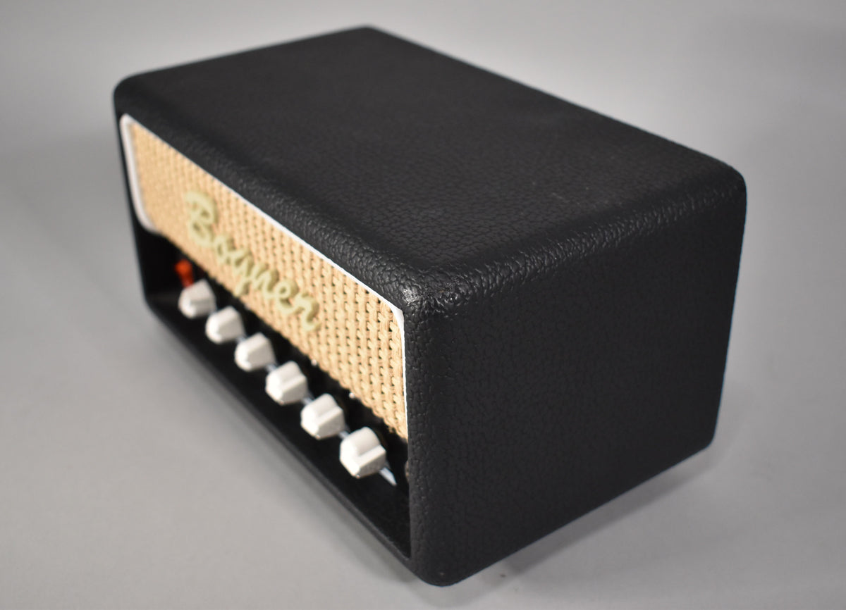 The black textured amp head is angled from the right, showing the front panel with a tan woven grille and six white knobs.