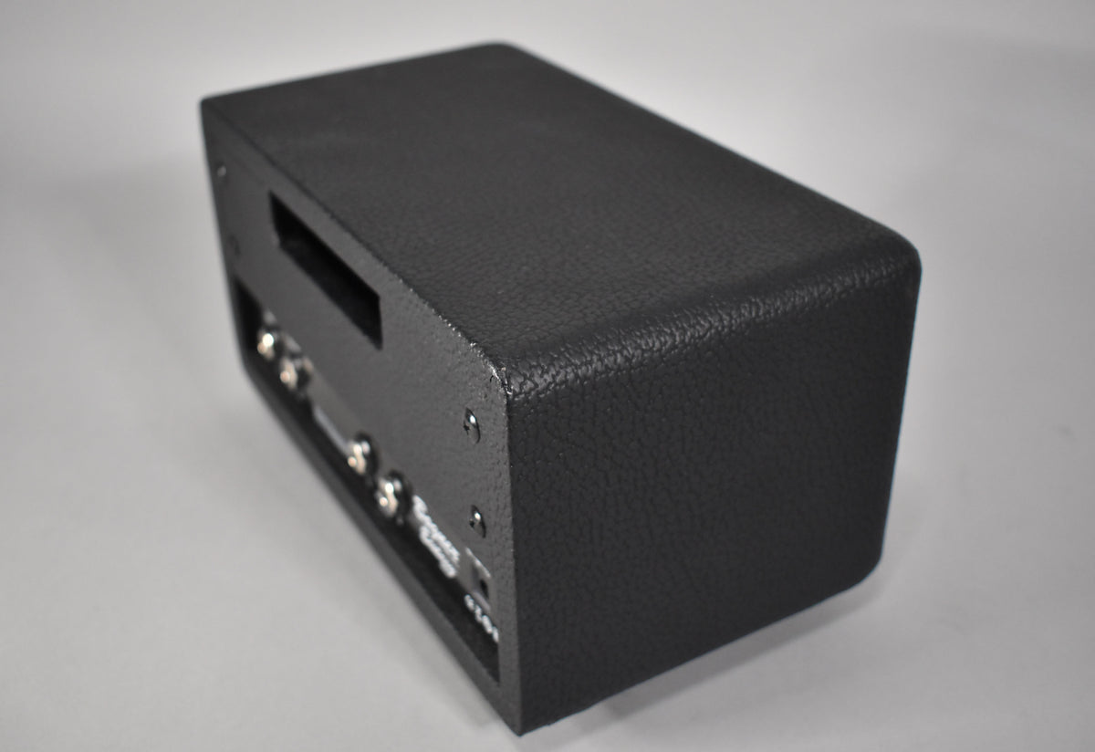 The black textured amp head is viewed from the top right, showing the front panel with several silver knobs and a small rectangular opening.