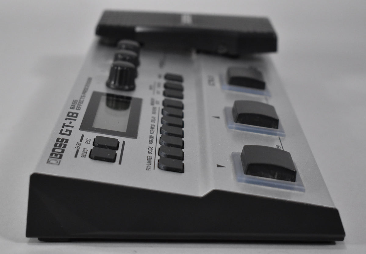 A silver multi-effects pedal is angled from the left, showing a screen, many black buttons, and three foot switches.
