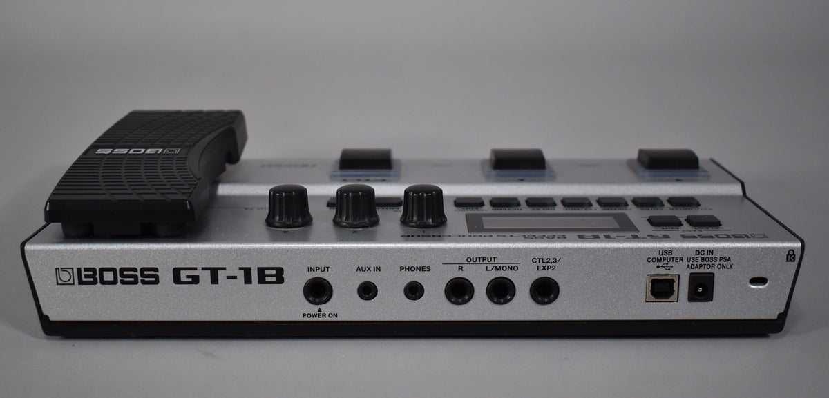 The silver multi-effect pedal is seen from the rear, showing the input/output jacks, USB port, and power input.