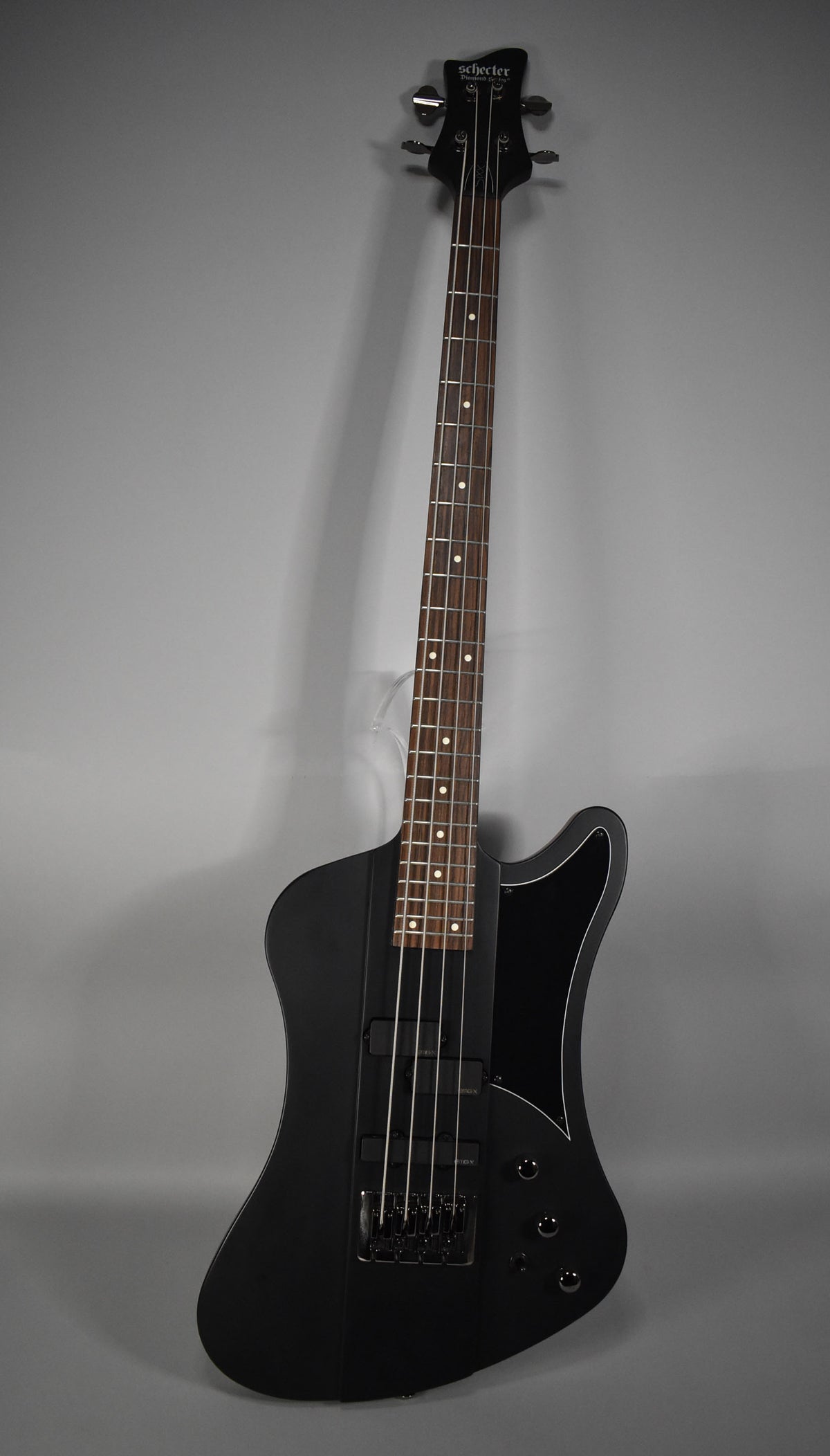 Full-length, slightly angled view of a satin black bass with a unique body shape, black hardware, and two humbucker pickups.