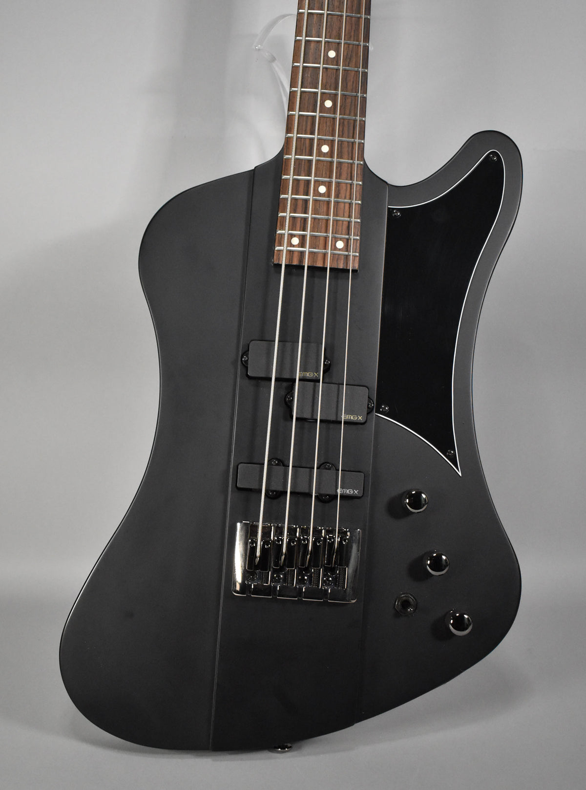 Close-up of a matte black bass, angled to show the body, dark fretboard with white dot inlays, and three black pickups.