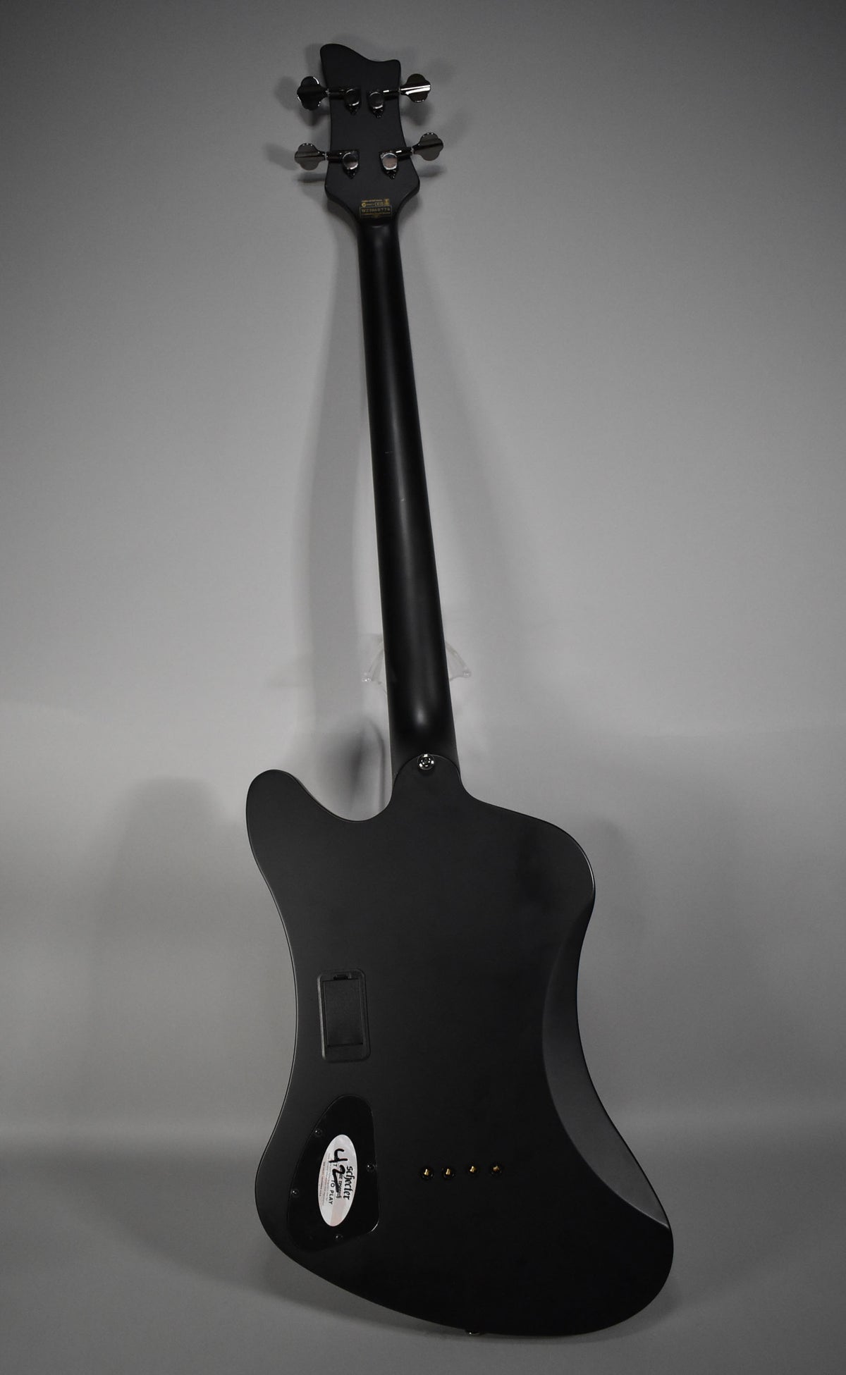 The bass's back is visible, showing a satin black finish, black hardware, and a white sticker on the control cavity cover.