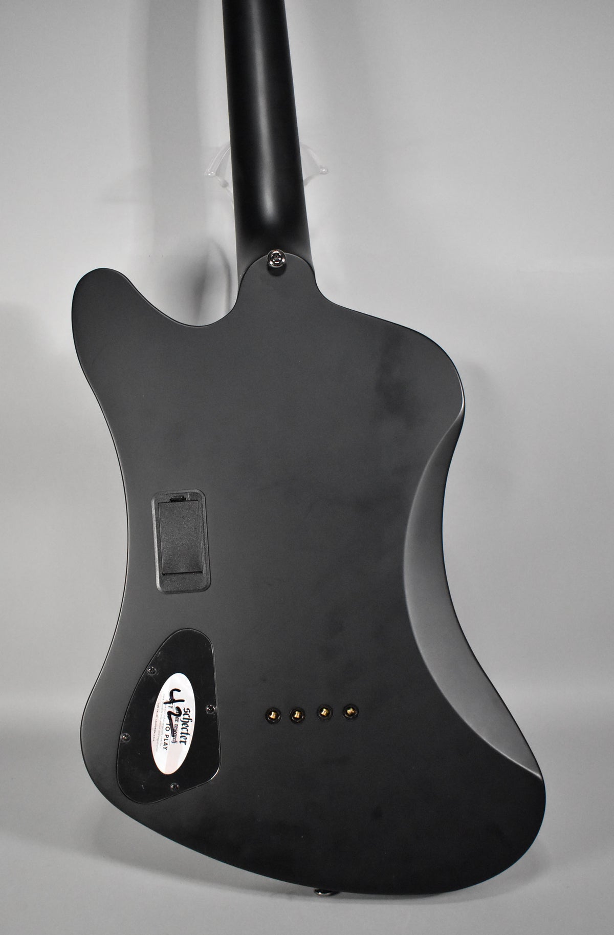Rear view of the matte black bass, showing the neck joint, battery compartment, control cavity, and four gold string ferrules.