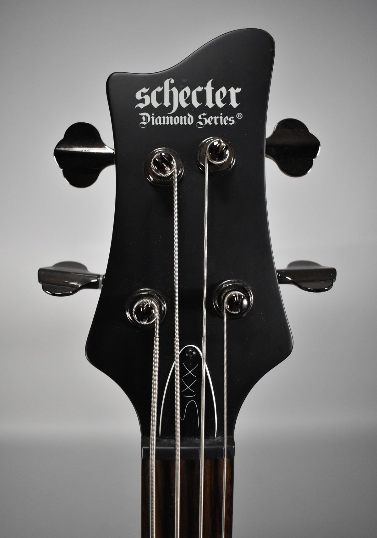 Close-up of the bass headstock, satin black with black tuners, showing the top two tuners on each side and the nut.