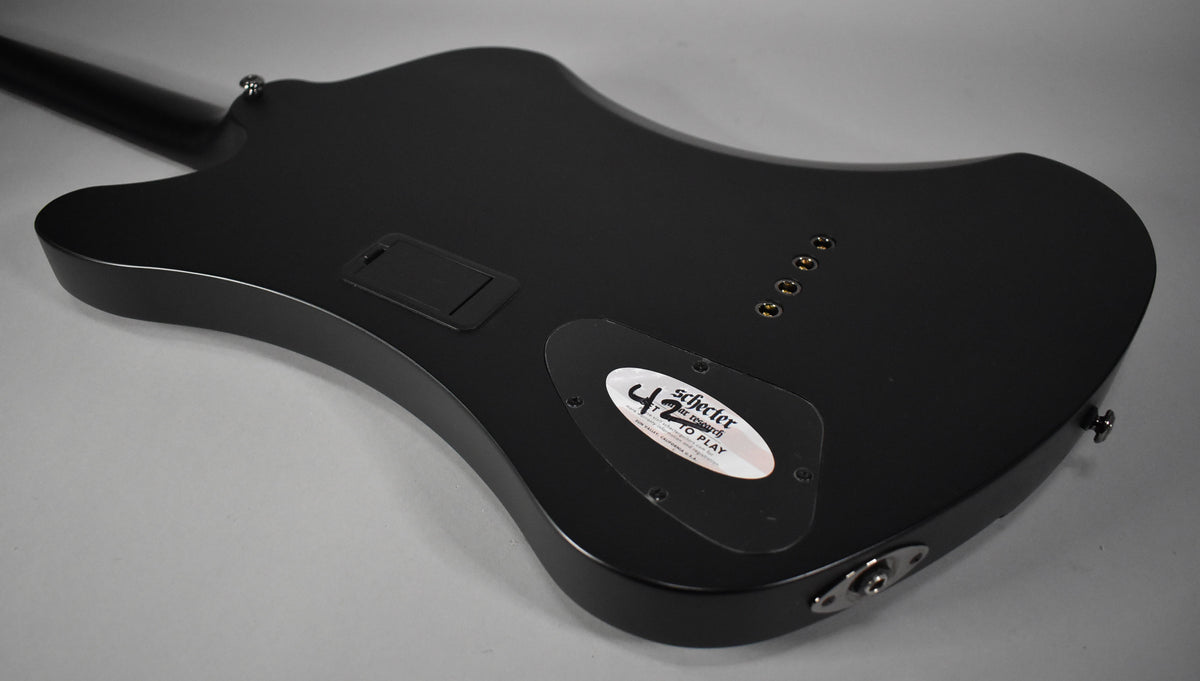 The bass's satin black body is seen from the back, angled right, revealing a battery compartment and control cavity cover.