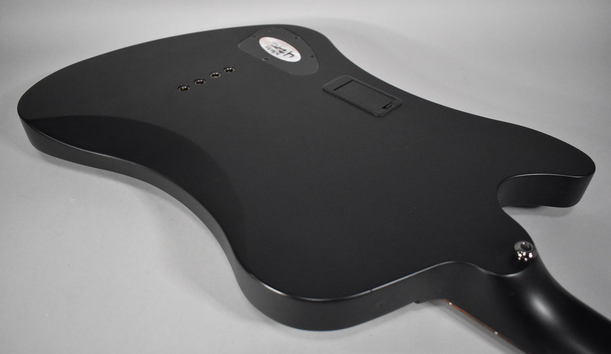 The bass's satin black body is seen from the back, angled left, showing the battery compartment and string-through-body ferrules.