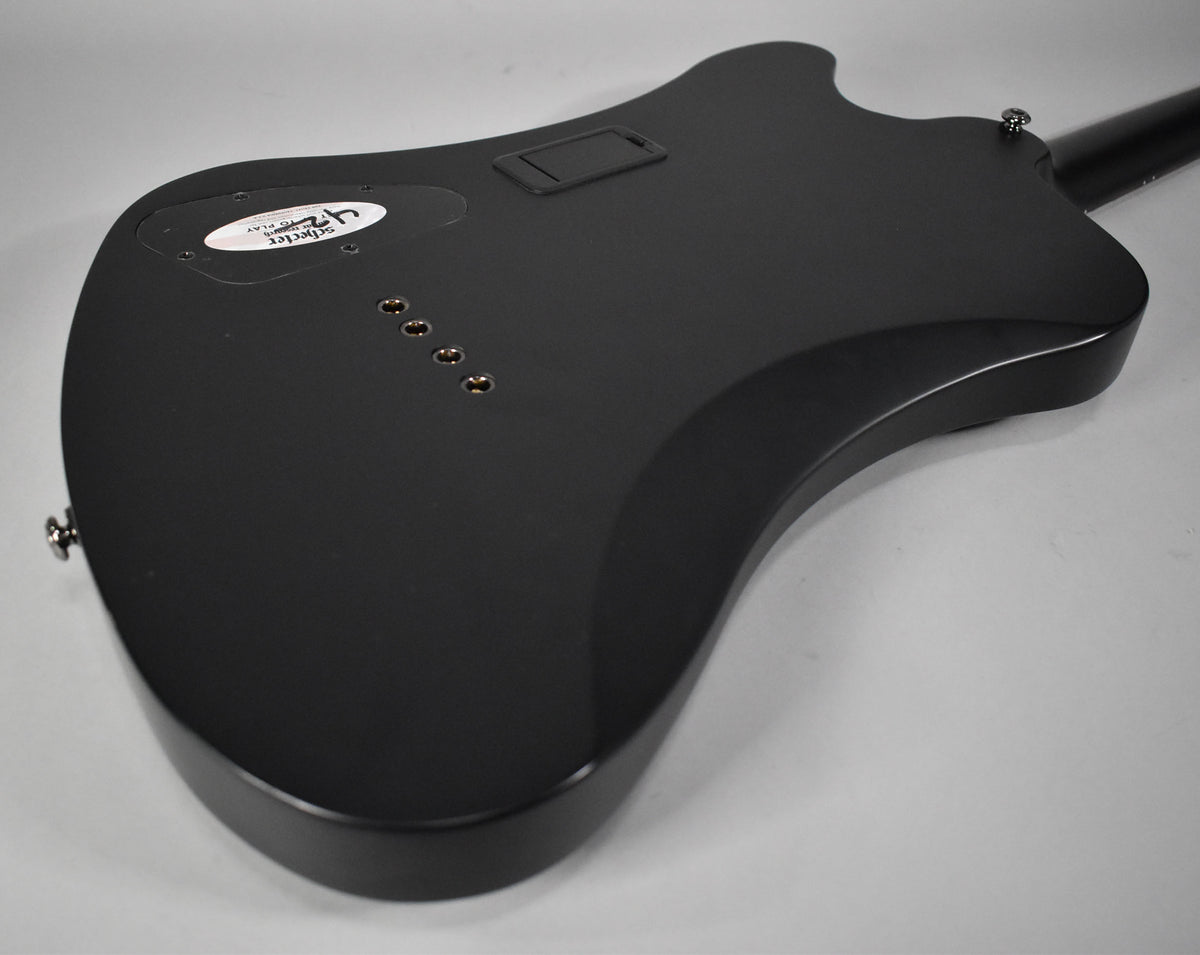 The back of a satin black bass guitar, angled from the lower bout, showing string-through ferrules and control cavity covers.