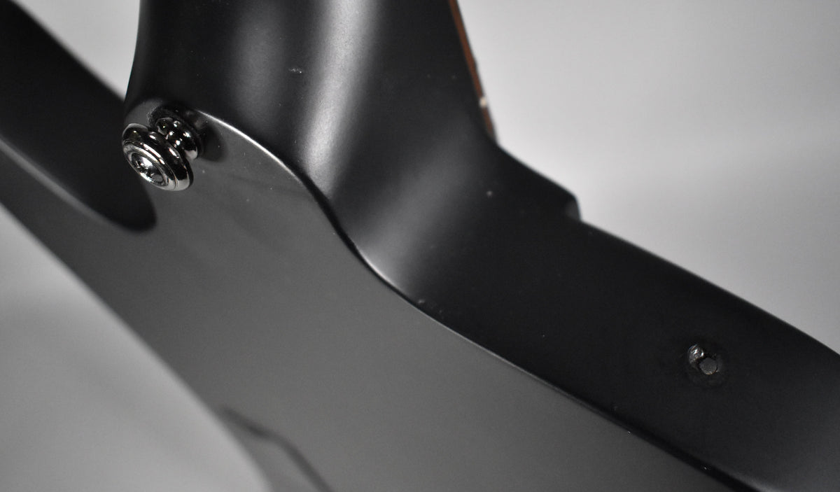 Close-up of the satin black bass body and neck joint, showing a chrome strap button and a small screw on the body.