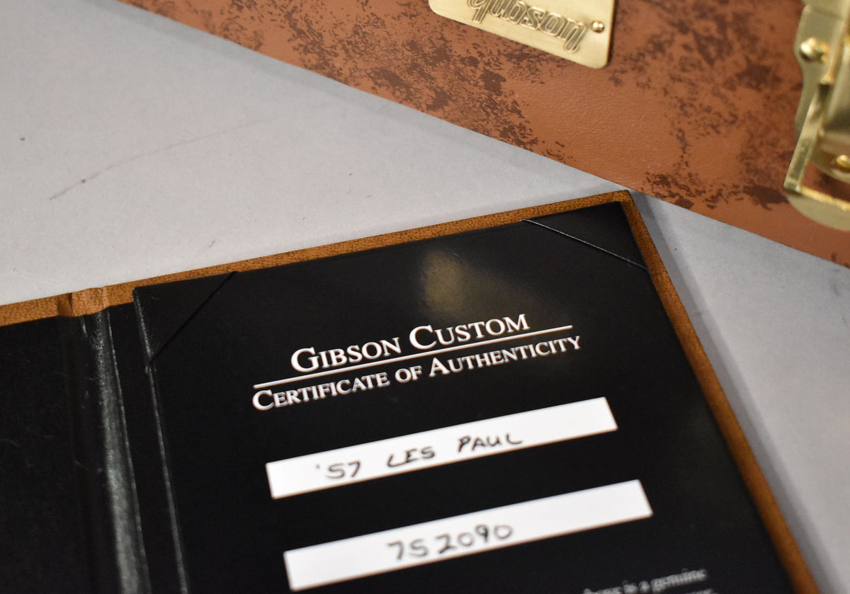 A black Gibson Custom Certificate of Authenticity for a '57 Les Paul, with a brown hard case partially visible.