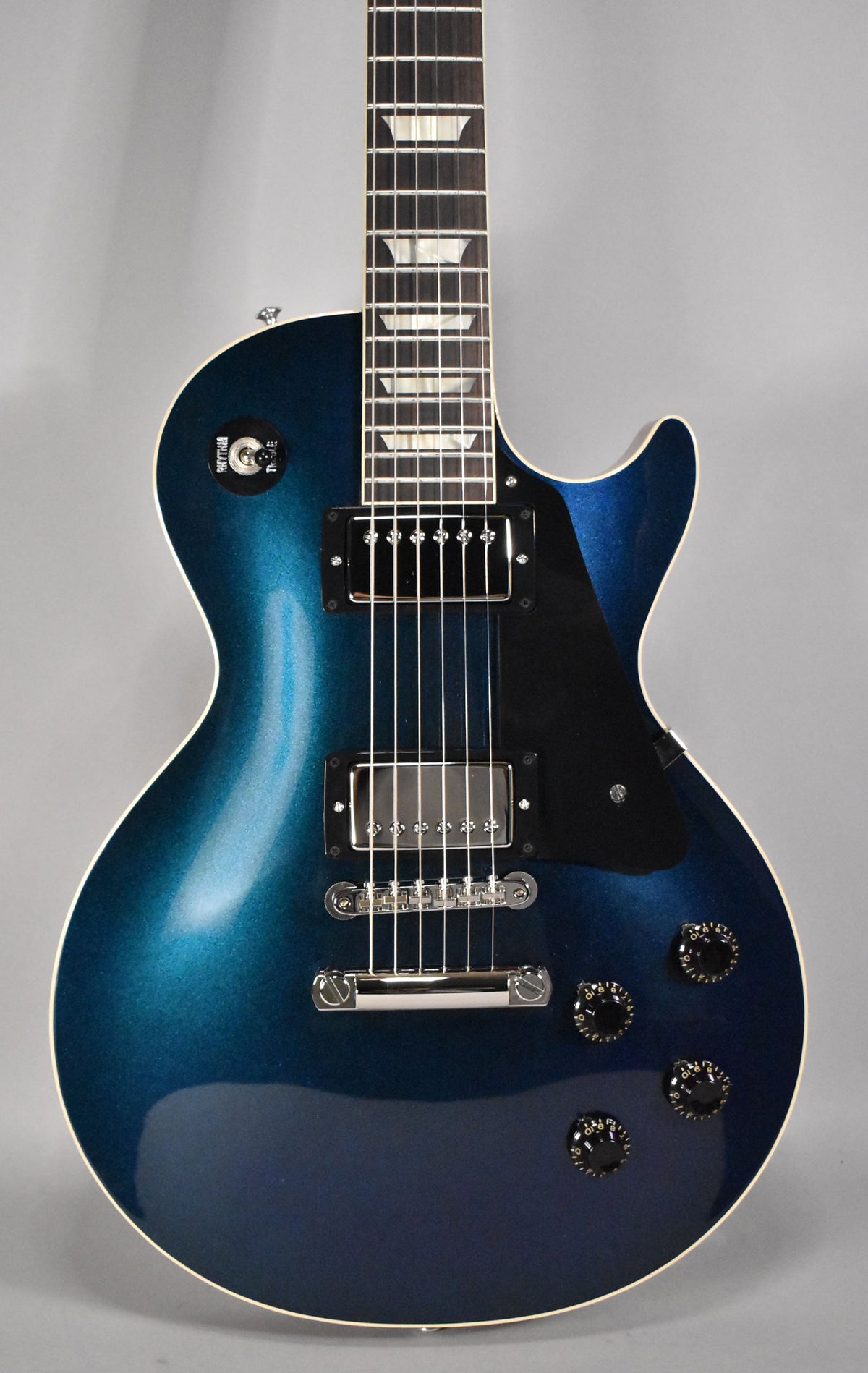 Full-frame, top-down view of a blue-to-dark-blue burst guitar with a black pickguard, two humbuckers, and four black control knobs.