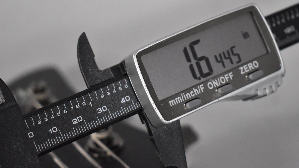 A digital caliper measures 1.6445 inches, with the jaws clamped around a guitar string.