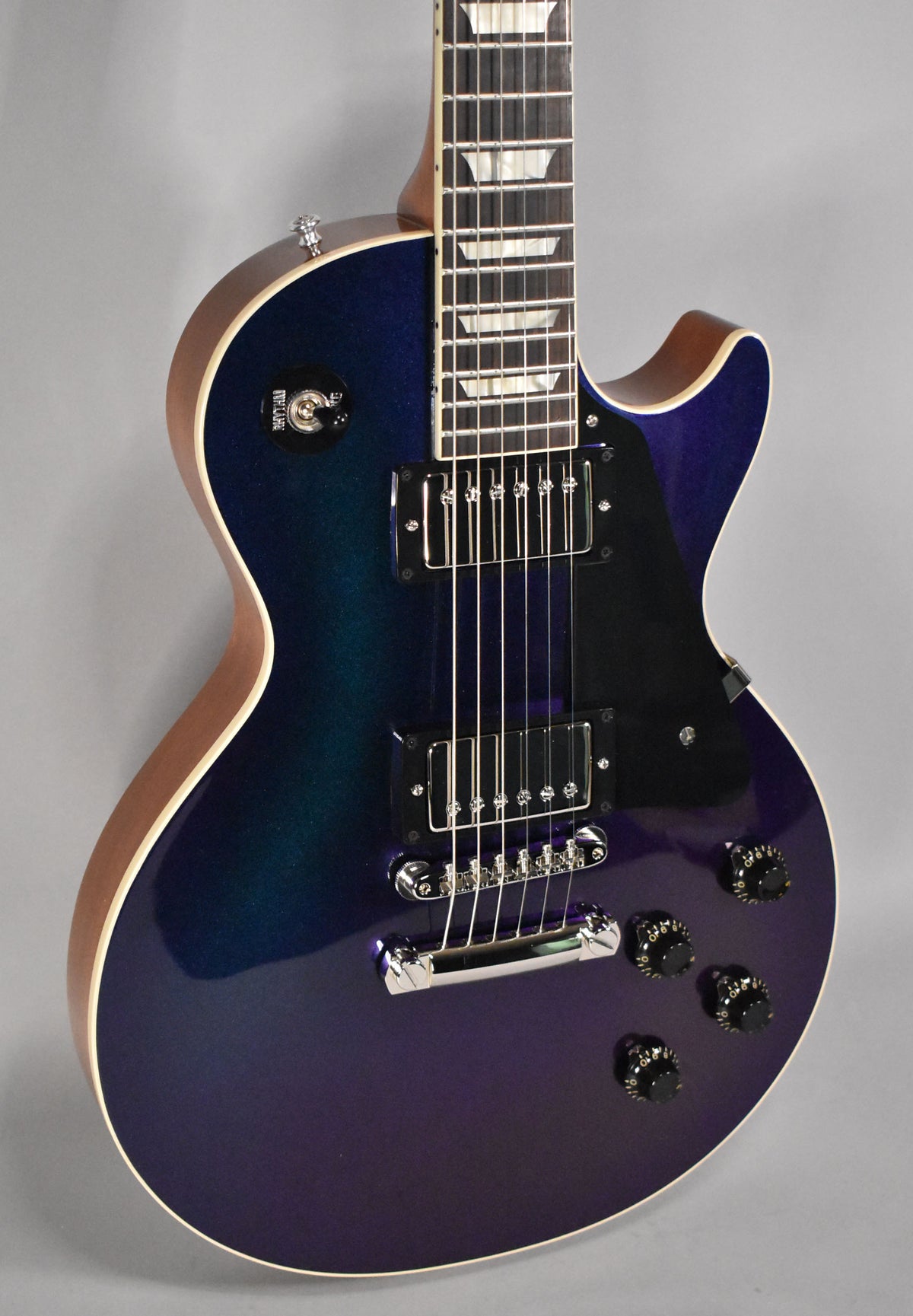 The guitar's body, angled from the neck to the lower bout, shows a blue-to-purple sparkle finish, black pickups, and chrome hardware.