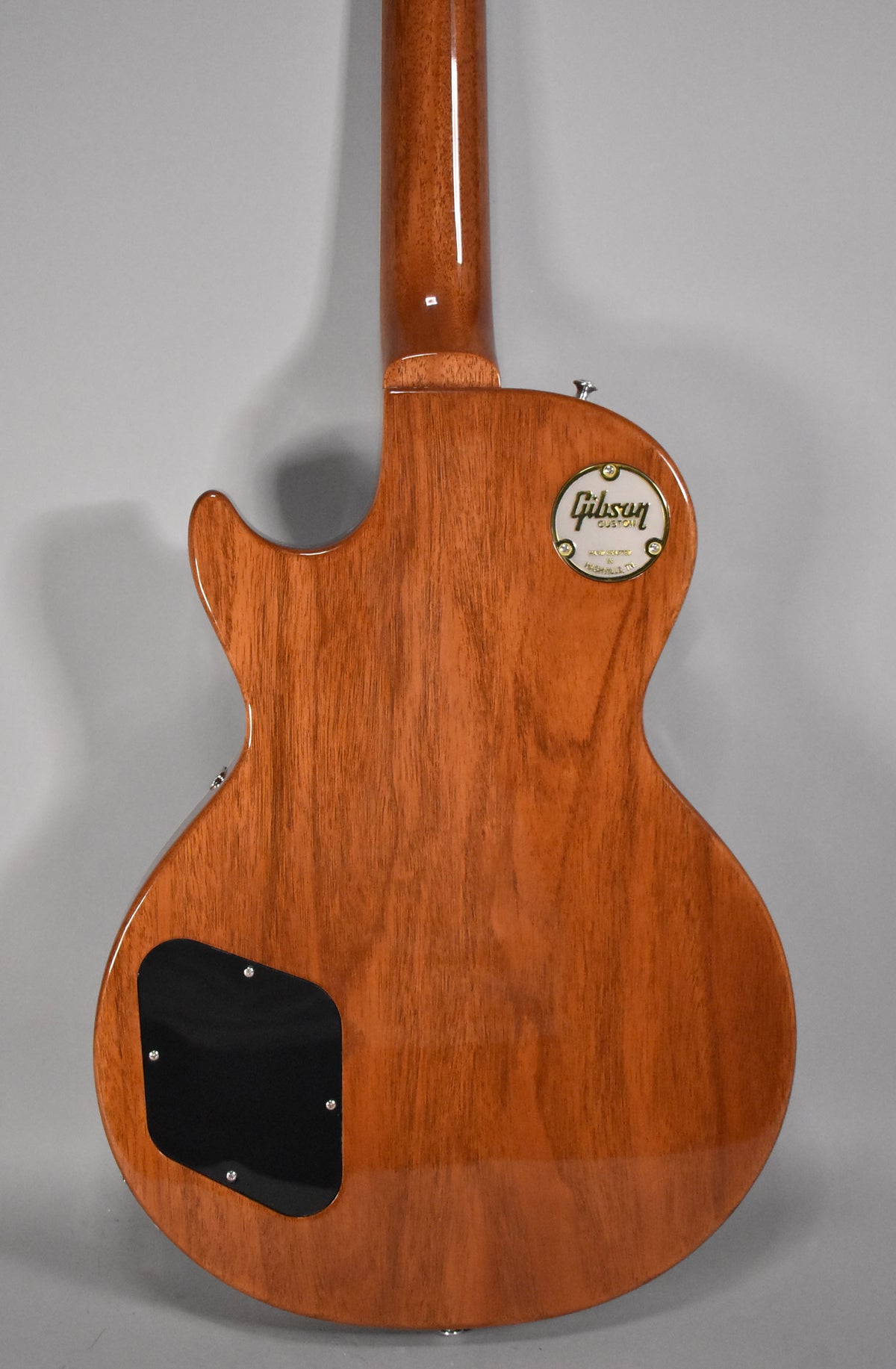 The guitar's back, neck, and headstock are visible, showing a glossy, reddish-brown wood grain finish with a black control cavity cover.