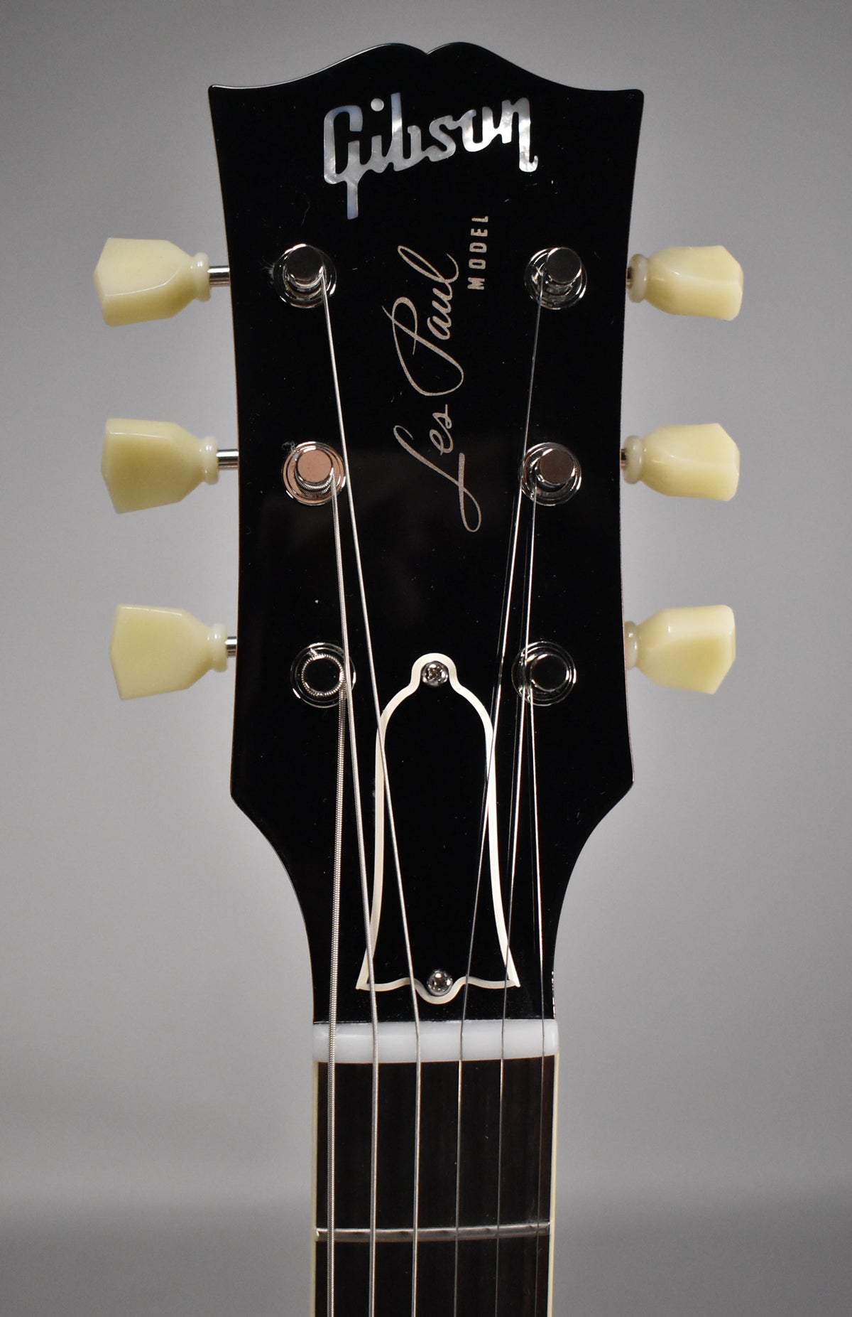 Close-up of a glossy black headstock with cream tuning pegs, a white nut, and a bell-shaped truss rod cover.