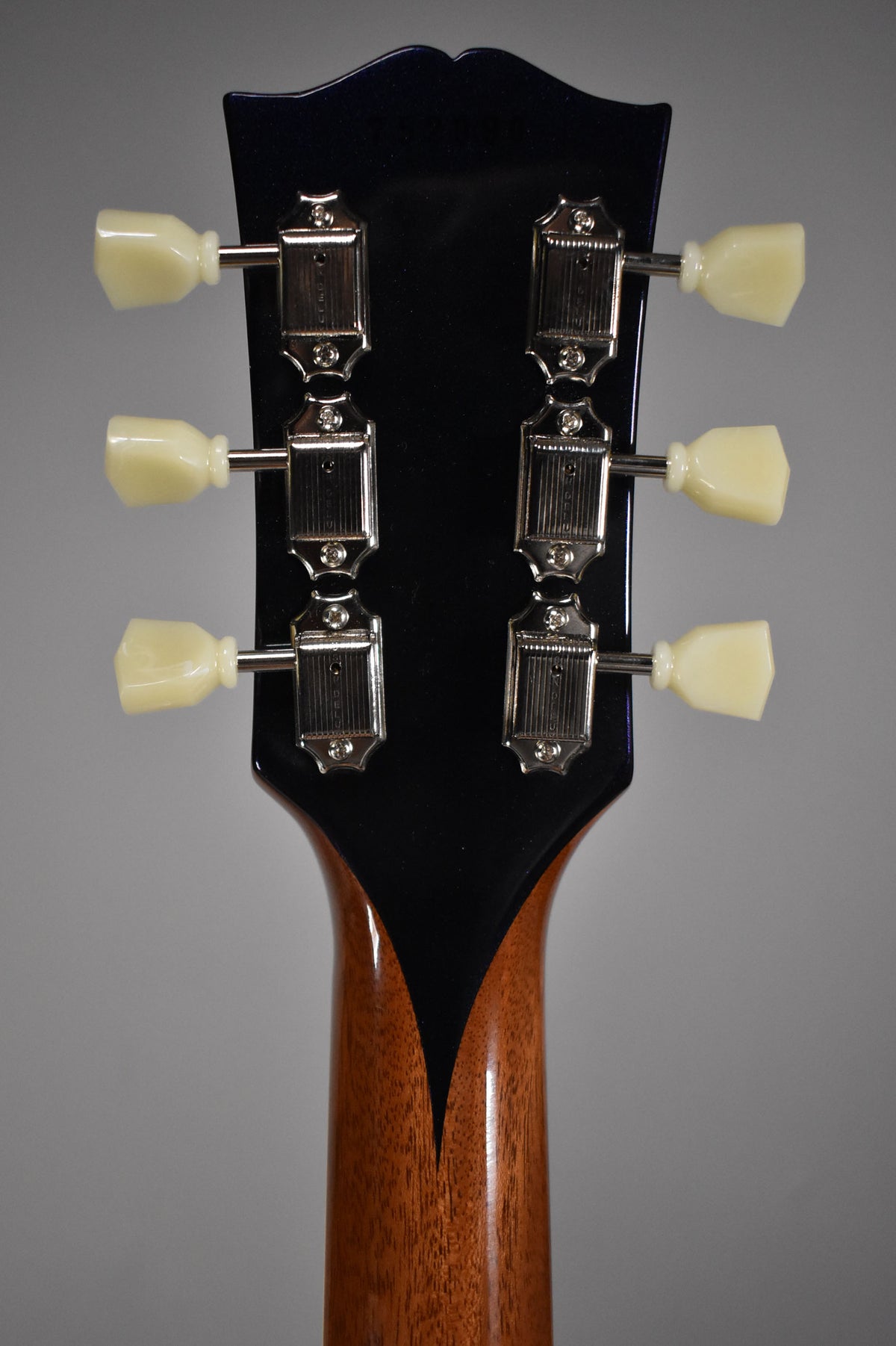 Rear view of the guitar's headstock, showing six cream tuning pegs on a glossy dark blue headstock and a mahogany neck.
