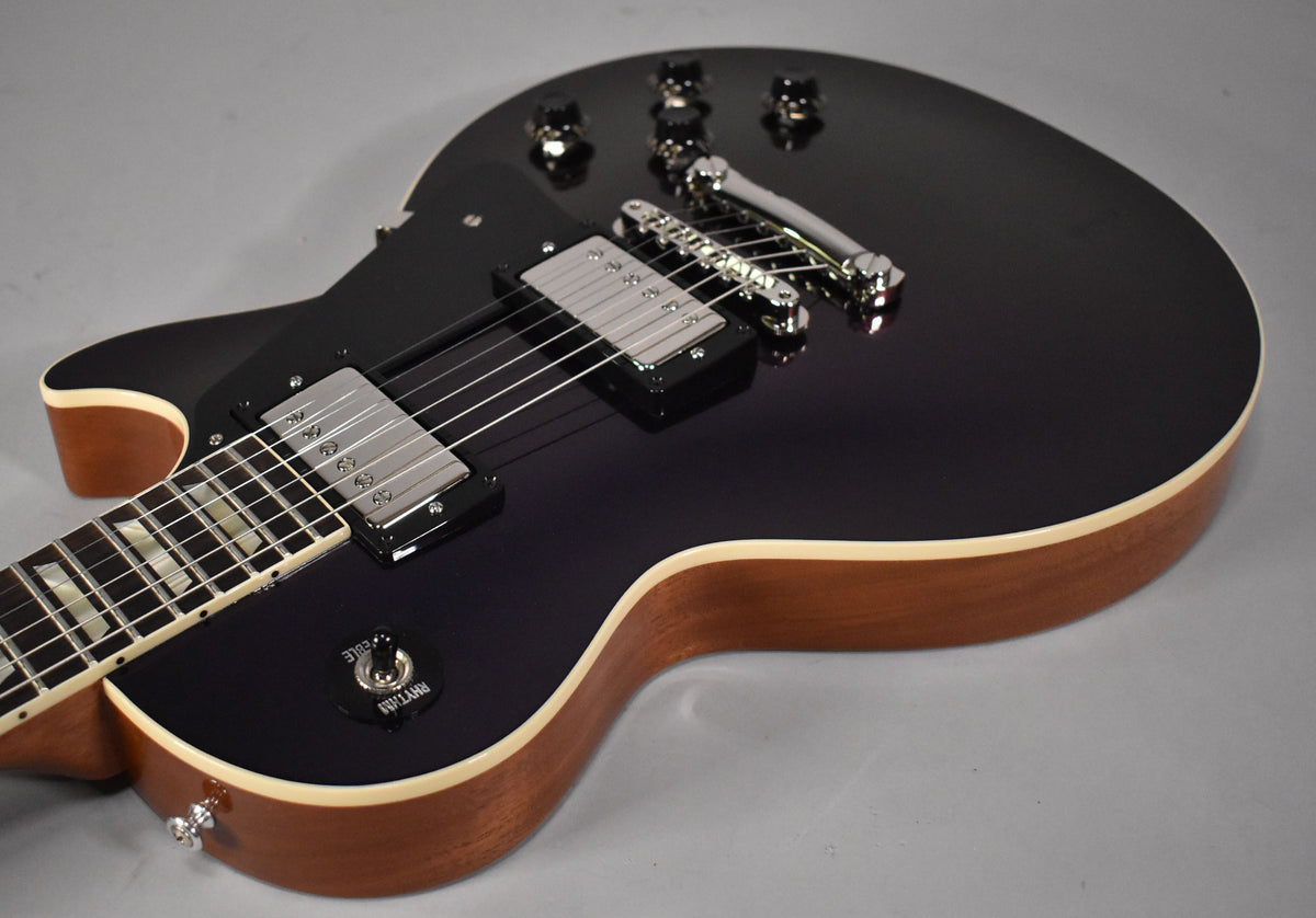 The upper body of a dark purple Les Paul, showing chrome hardware, black pickup rings, and a natural wood side with cream binding.