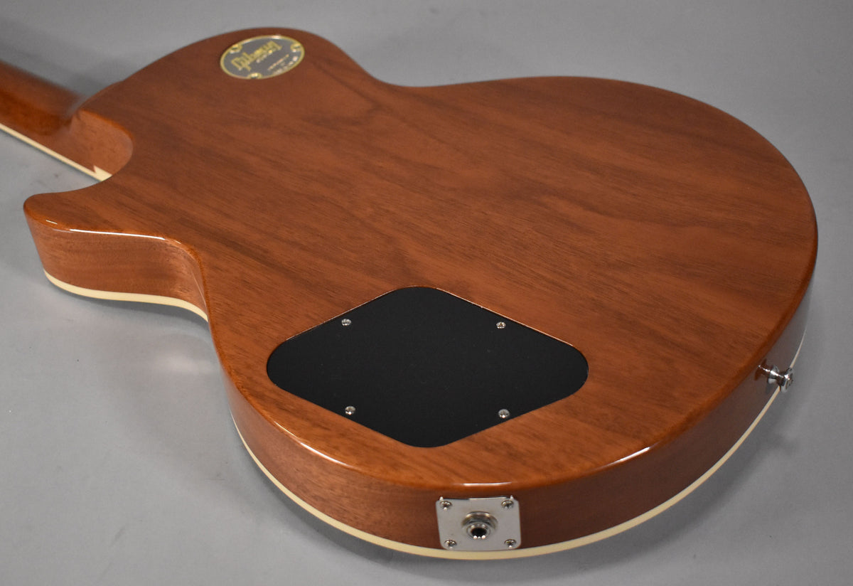The back of a glossy, light brown guitar body with cream binding, a black control cavity cover, and a chrome output jack.