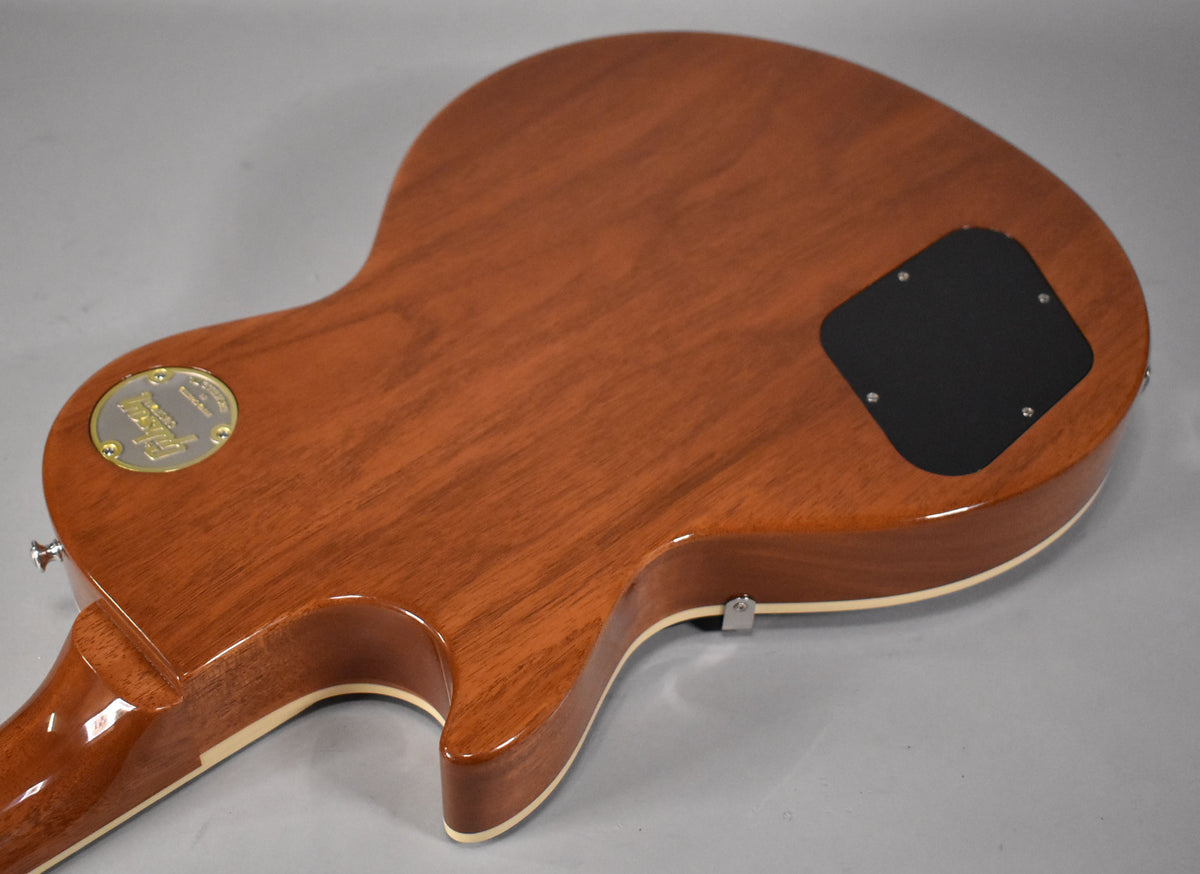The back of the Les Paul shows a glossy, reddish-brown finish with wood grain, a black control cavity cover, and a gold medallion.