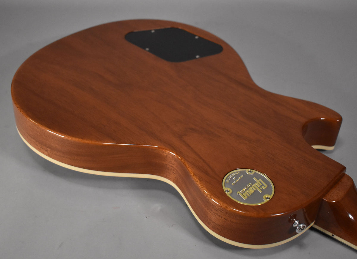 The back of a Les Paul guitar, showing its glossy reddish-brown finish, cream binding, and a black control cavity cover.