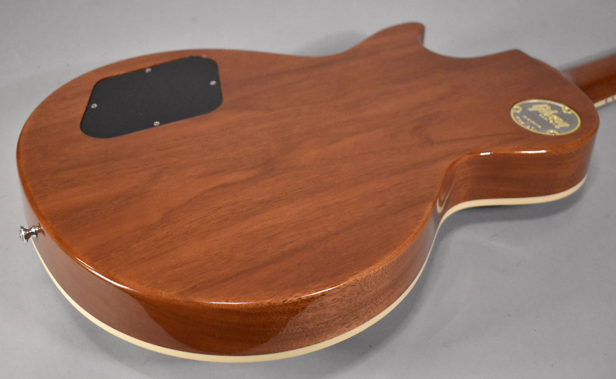 The back of a glossy, reddish-brown electric guitar, showing a black control cavity cover and a gold Gibson Custom Shop decal.