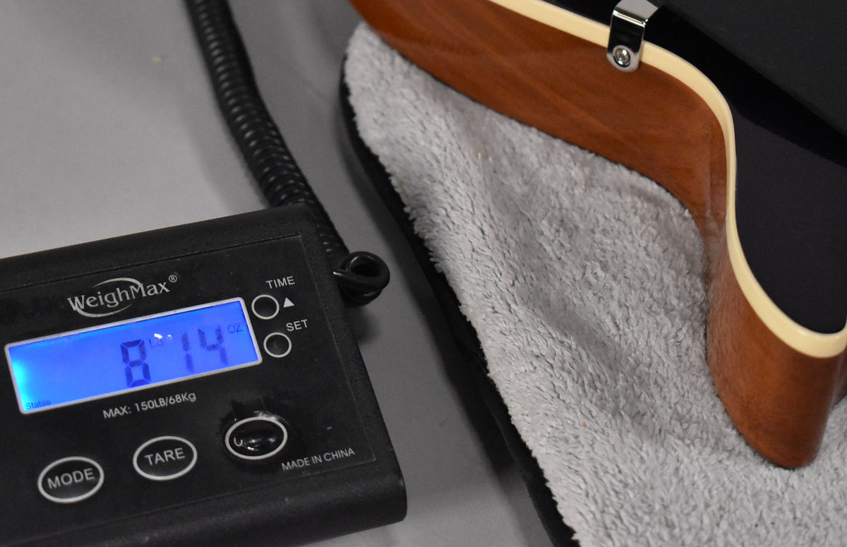 The guitar's lower bout and neck heel rest on a grey plush case lining, with a scale displaying "8 LB 14 OZ" to the left.