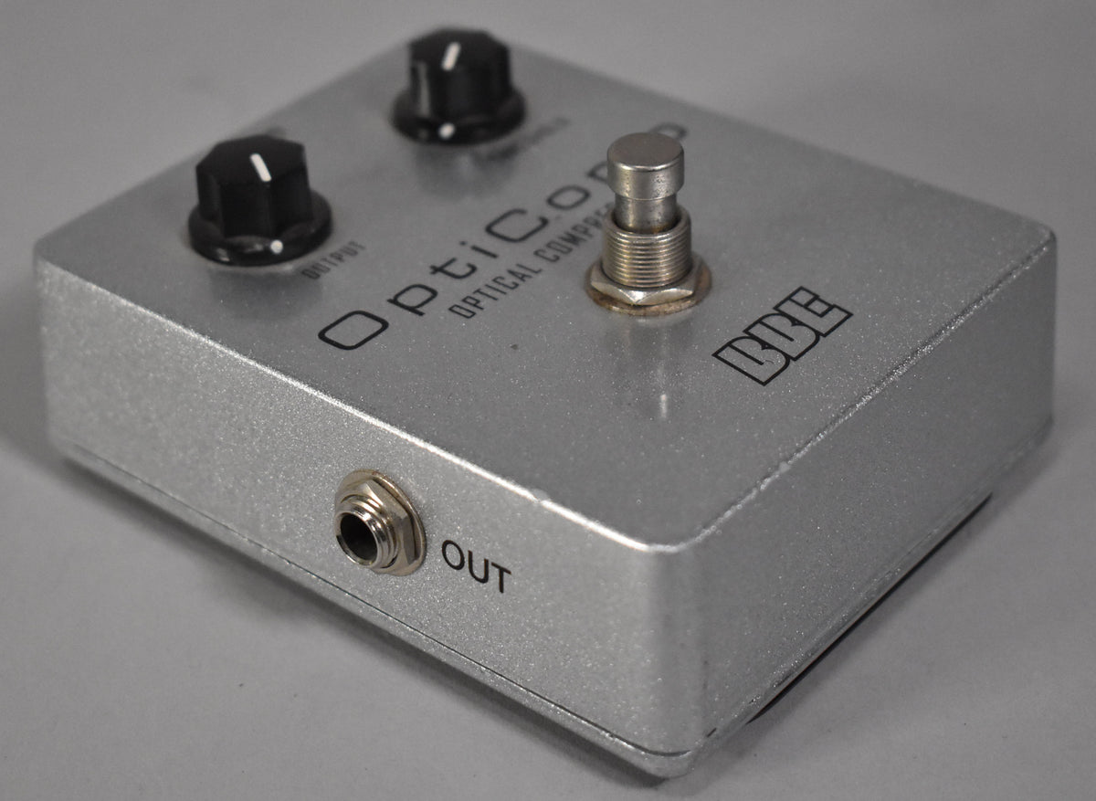 A silver guitar pedal, viewed from the front-right, with two black knobs, a metal footswitch, and an "OUT" jack.