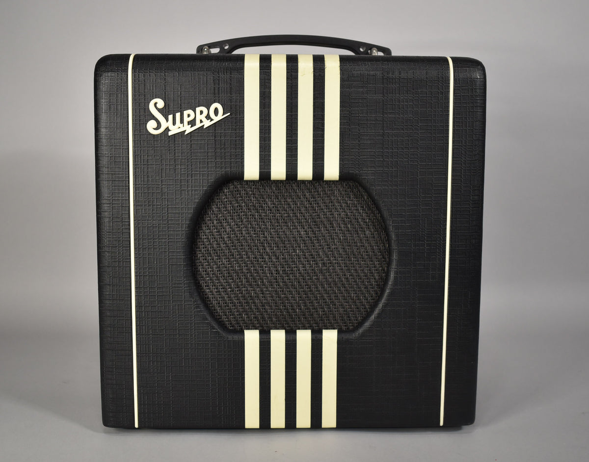 Front view of a black textured amp with a cream "Supro" logo, three vertical cream stripes, and a round speaker grille.