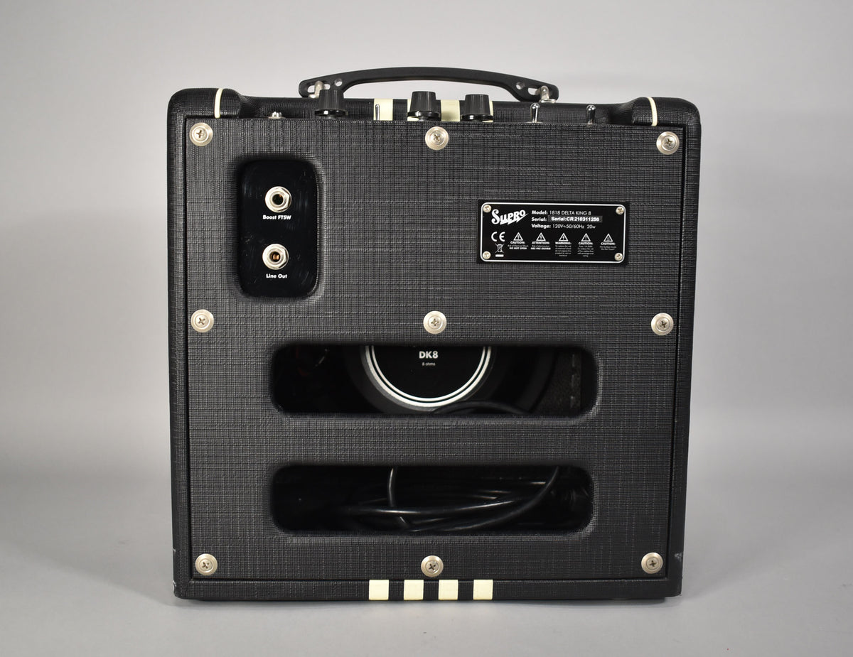 The black textured combo amp's back panel shows two open ports, a label, and two rectangular cutouts revealing the speaker and cables.