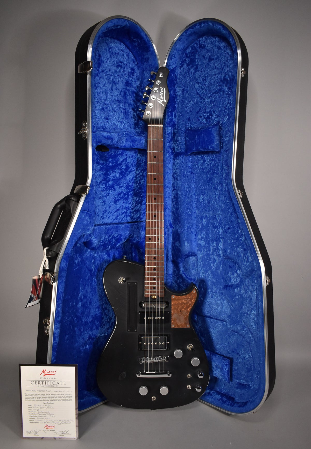 Full-length view of a black relic electric guitar with a wood pickguard, in a blue-lined hard case, with a certificate.