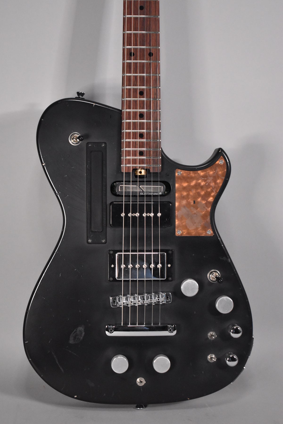 The black relic electric guitar's body and lower neck are visible, showing a copper pickguard, two humbuckers, and six silver control knobs.