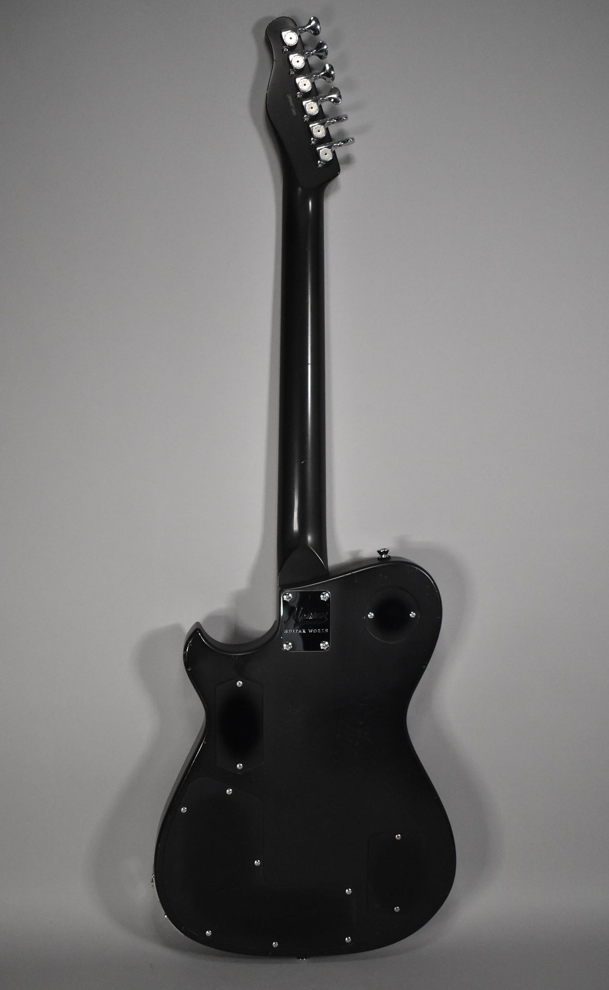 The guitar's black body and neck are viewed from the back, showing six chrome tuners and a neck plate.