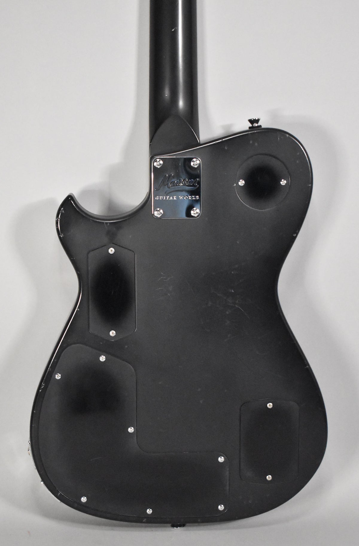 The back of a black relic guitar, showing the neck joint, control cavity covers, and strap button.
