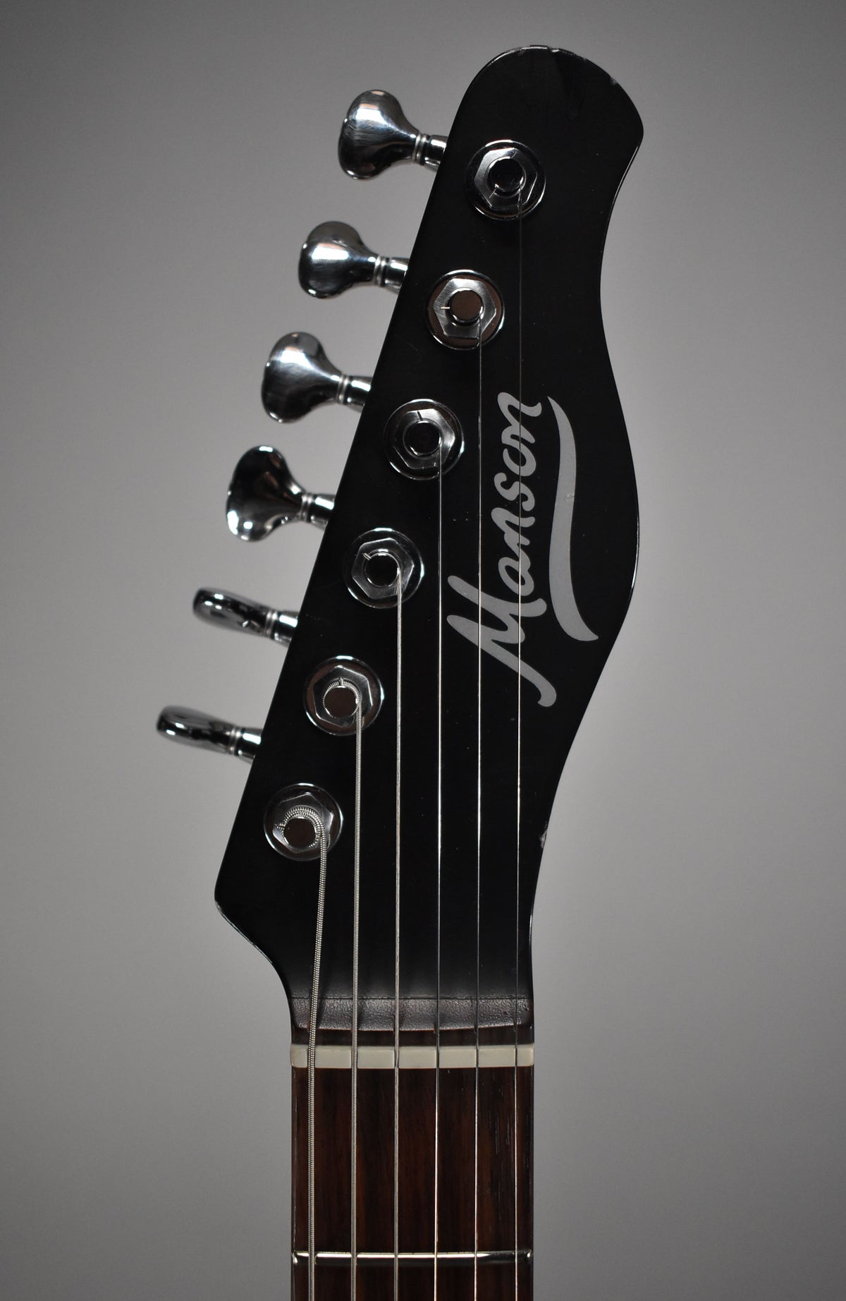 Close-up of the black headstock with six chrome tuners, showing a small chip on the top edge and a relic'd finish.