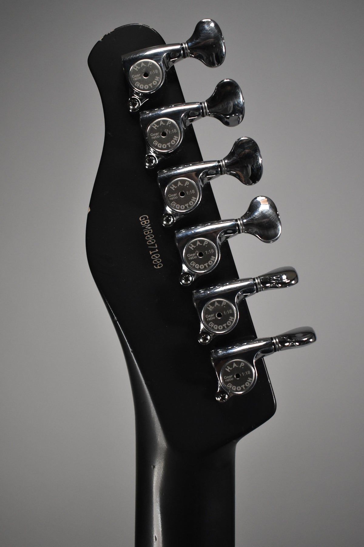 The back of a black headstock with six chrome tuners, showing light wear and a serial number.