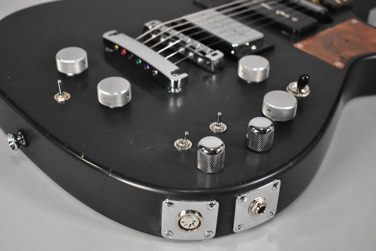 Close-up of the matte black body, showing six knurled chrome knobs, four toggle switches, and two output jacks on the lower bout.