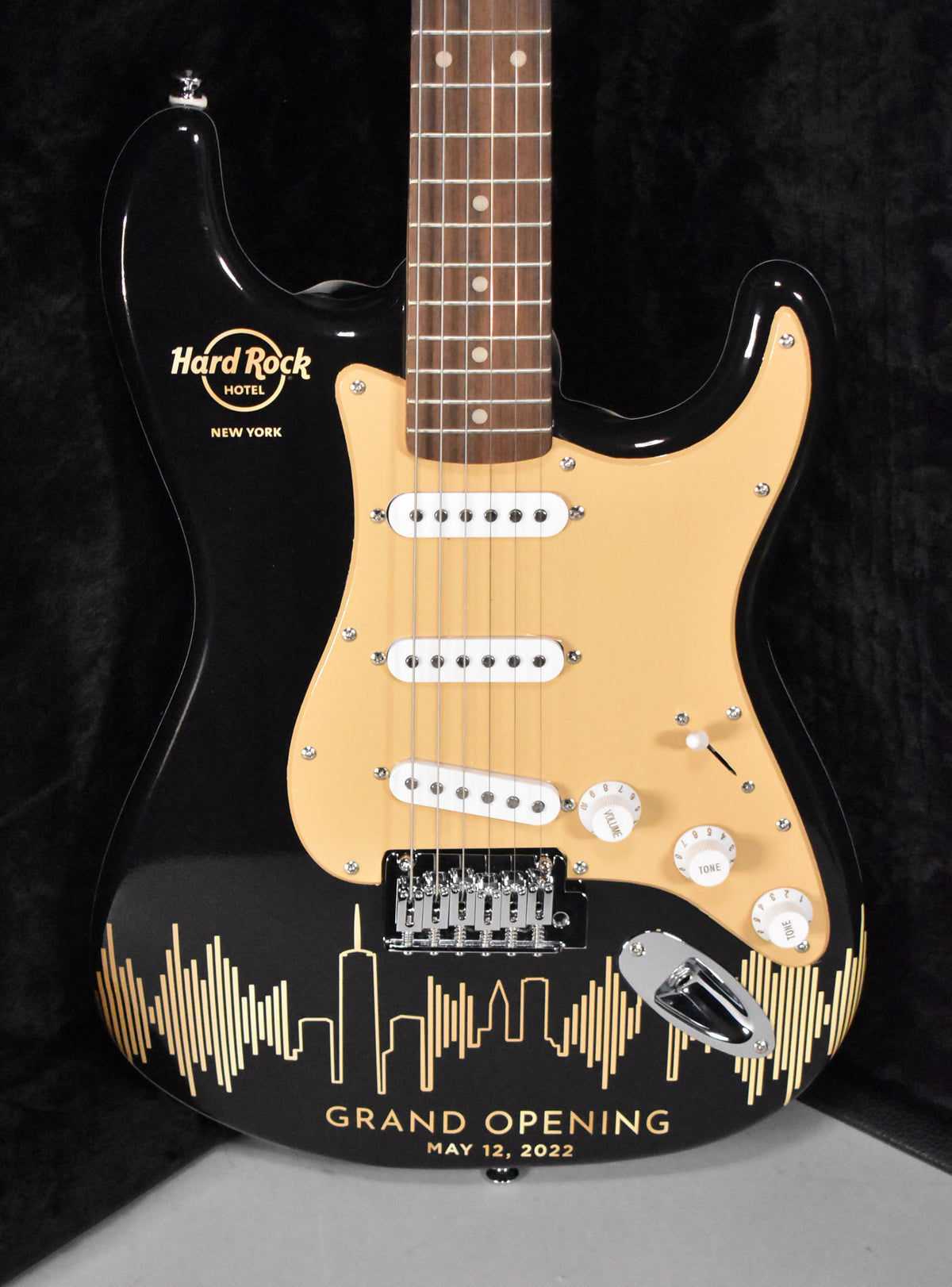Full front view of a black Stratocaster with a cream pickguard, three white single-coil pickups, and gold Hard Rock Hotel NYC branding.