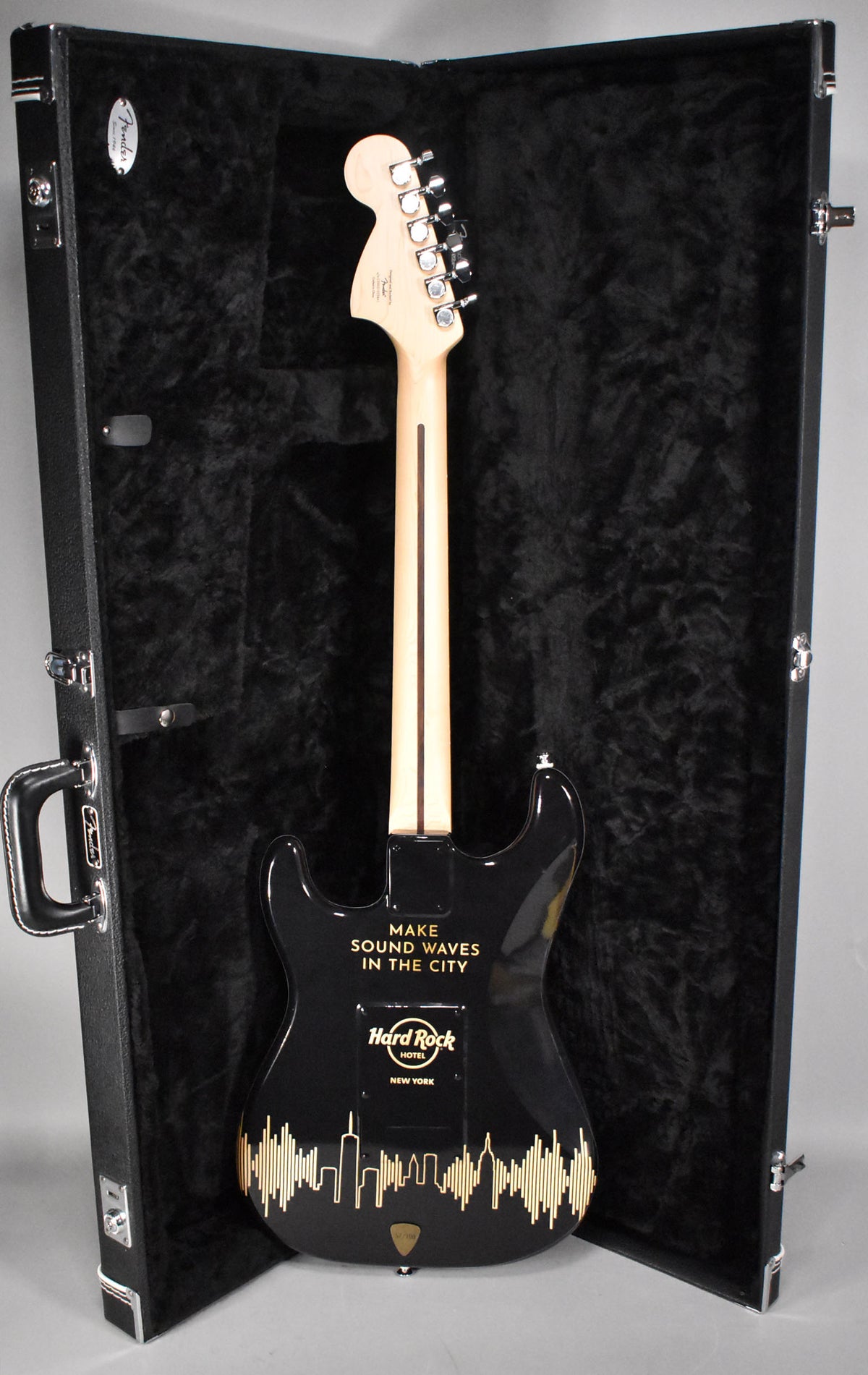The back of a black Stratocaster with "MAKE SOUND WAVES IN THE CITY" and "Hard Rock Hotel NEW YORK" in gold, in a black hard case.