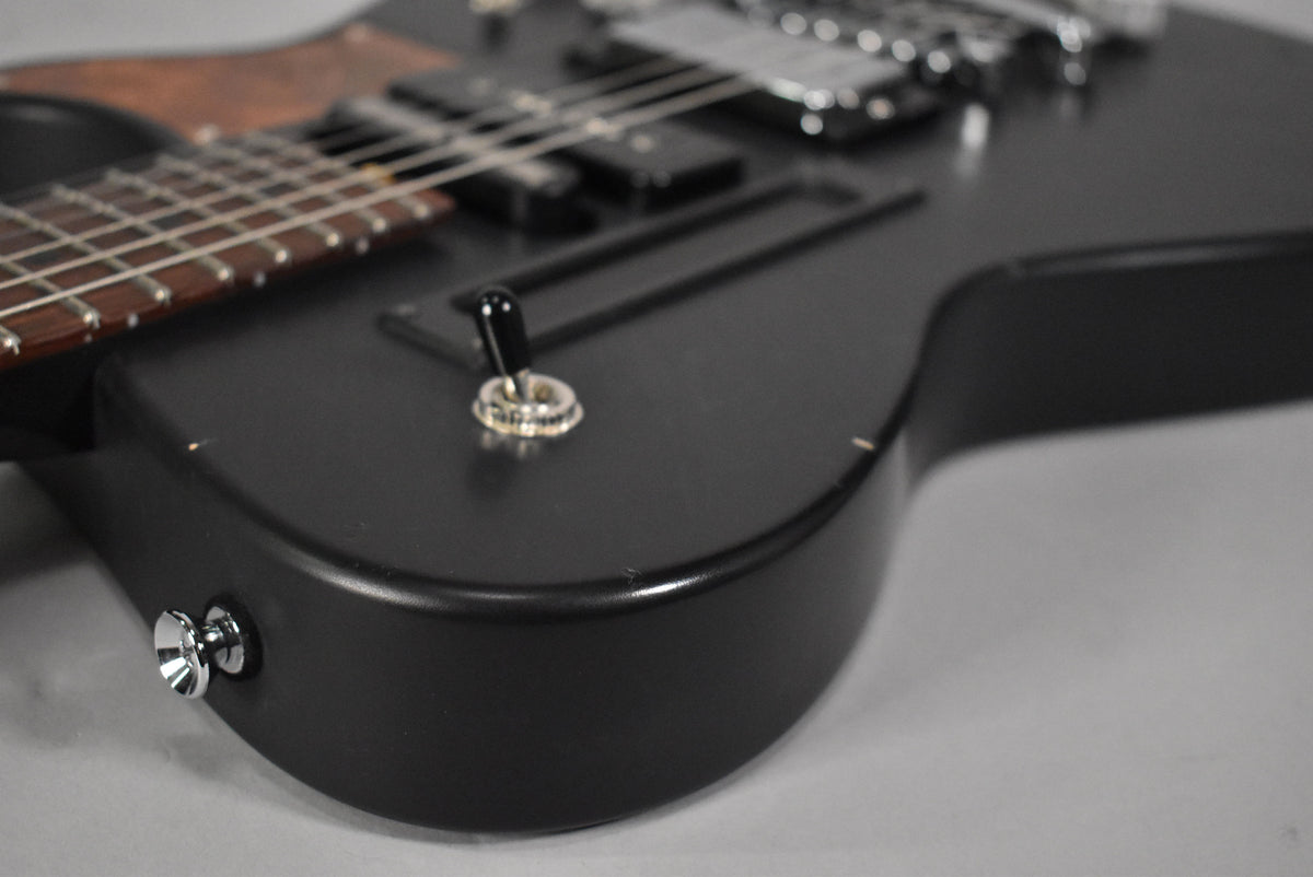 Close-up of the matte black guitar body's lower bout, showing the chrome strap button, pickup selector switch, and light relic wear.