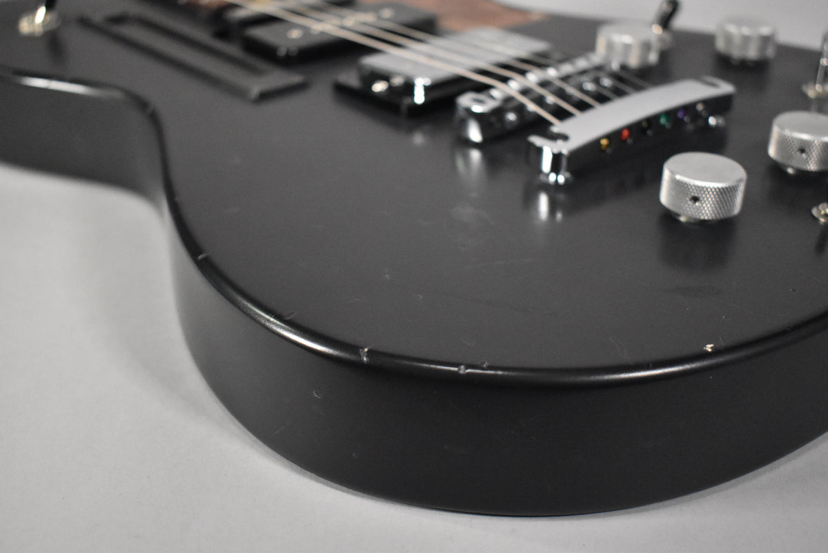 Close-up of the guitar's lower bout, showing the matte black finish with light scratches, chrome hardware, and knurled control knobs.