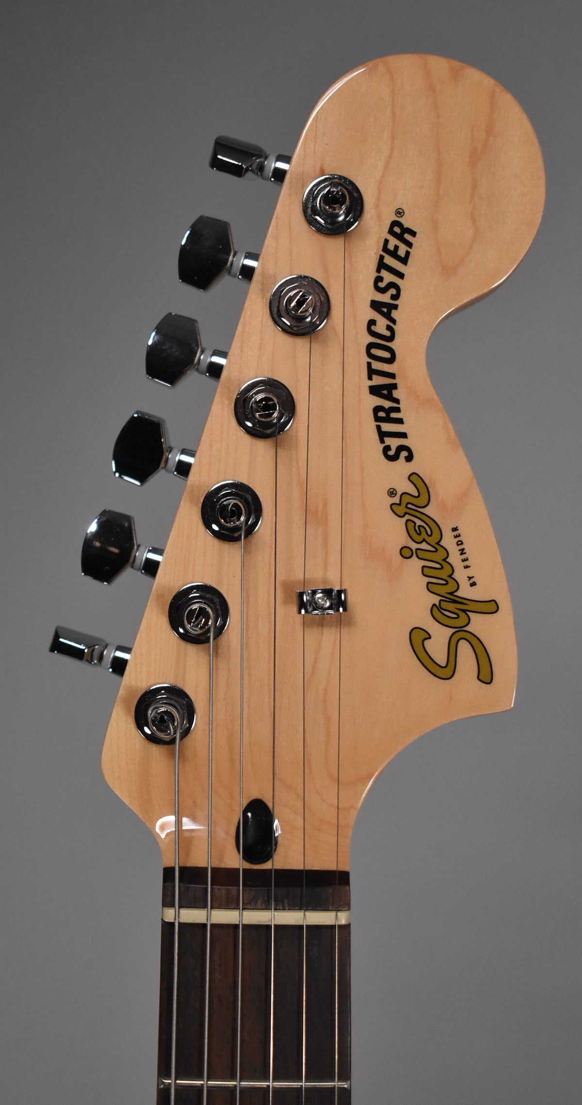 Close-up of the guitar's light wood headstock with six chrome tuners, a string tree, and a dark nut, showing the top of the dark fretboard.